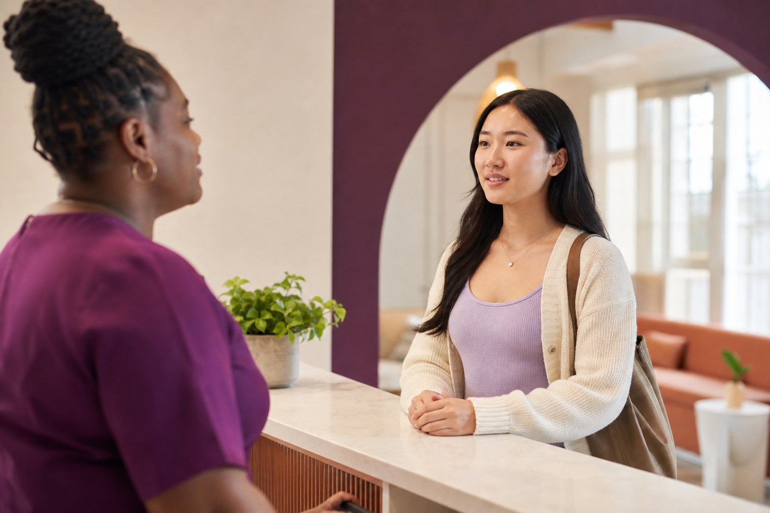 Young Asian woman speaking with a welcoming Black clinic staff member at reception